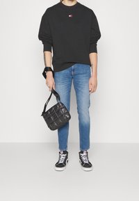 Svart sweatshirt med liten logotyp, blå jeans, svart quiltad axelväska och svarta högkängor med vita snören.