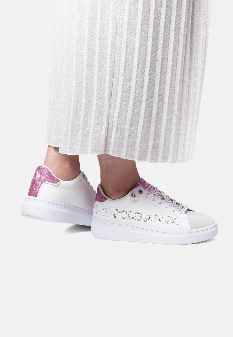 Weiße Sneakers mit pink glitzernden Absätzen und Schnürsenkeln, U.S. Polo Assn. Branding, getragen zu einem langen weißen plissierten Rock.