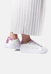 Vita sneakers med en slät yta, rosa glitterdetaljer på hälen och perforerad varumärkesdetalj på sidan. Platt vit sula.