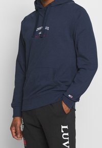 Mörkblå hoodie från Tommy Jeans med framficka, justerbar dragkedja på huvan och broderad logotypdetalj på bröstet.