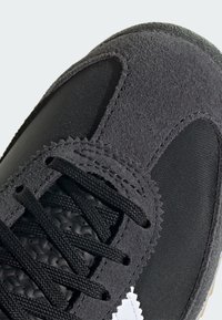 Zapatilla negra con parte superior de ante, paneles de malla y suela texturizada. Los cordones negros completan el diseño, con un acento en logo blanco.