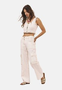 Top blanco recortado con borde de encaje, combinado con pantalones cargo de cintura alta que cuentan con bolsillos laterales. Llevado con sandalias de color claro.