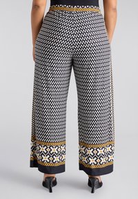 Zwarte wijde broek met een patroon van witte hartvormen, een geometrische gele en witte onderband, en een elastische taille.