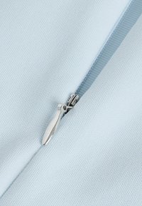 Hellblaues Gewebe mit einer strukturierten Oberfläche und einem silbernen Reißverschlussdetail, das ein schlankes, aerodynamisches Design aufweist. Der Reißverschlussgriff ist verlängert und aus Metall.