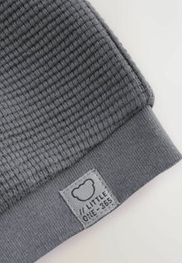 Close-up of gray knit fabric with a ribbed cuff and a sewn label featuring a bear outline and text "LITTLE ONE-365".