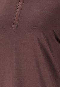 Mørkerød atletisk skjorte, kort lynlås ved kraven, letvægtsstof, glat tekstur, har "ENDURANCE" branding i subtilt print.