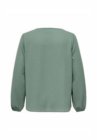 Garām piedurknēm, apaļa kakla izgriezuma krekls no teksturēta salvijas zaļā auduma. Rotāts ar savilktām aprocēm un taisnu apakšu, izstrādāts ērtai un brīvai piekļuvei.