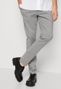 Šedé kostkované kalhoty na míru s úzkým střihem, rovně příčným pasem a jemnou texturou. Spárovány s černými šněrovacími botami s robustními podrážkami.