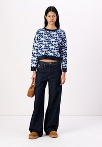 Crochet heart-patterned sweater in blue tones, paired with high-waisted dark denim wide-leg jeans, and brown slip-on shoes.