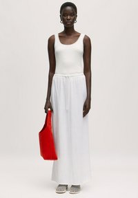 Witte linnen maxi rok met elastische taille, gecombineerd met een aansluitend wit tanktop. Houdt een rode stoffen handtas vast. Zwart-witte gestreepte schoenen.