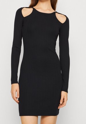 Czarna prążkowana dzianinowa sukienka z długim rękawem i odsłoniętymi ramionami, dopasowana sylwetka sięgająca połowy uda na stojącym modelu.