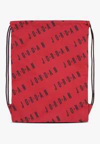 Crvena torba na vezanje izrađena od tkanine, s ponovljenim crnim natpisom "JORDAN". Jednostavnog pravokutnog oblika s crnim vezicama sa strane.