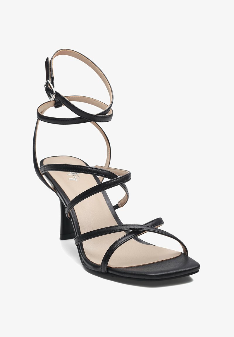 Musta remmillä varustettu korkokenkä, jossa on neliön muotoinen kärki ja joustavat remmit. Litteä nahkamainen materiaali, jossa on kontrastivärinen beige pohjallinen.