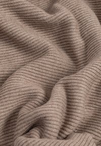 Tissu tricoté couleur brun clair avec une texture à fines côtes, présentant de douces ondulations et un subtil jeu de lumière et d'ombre.