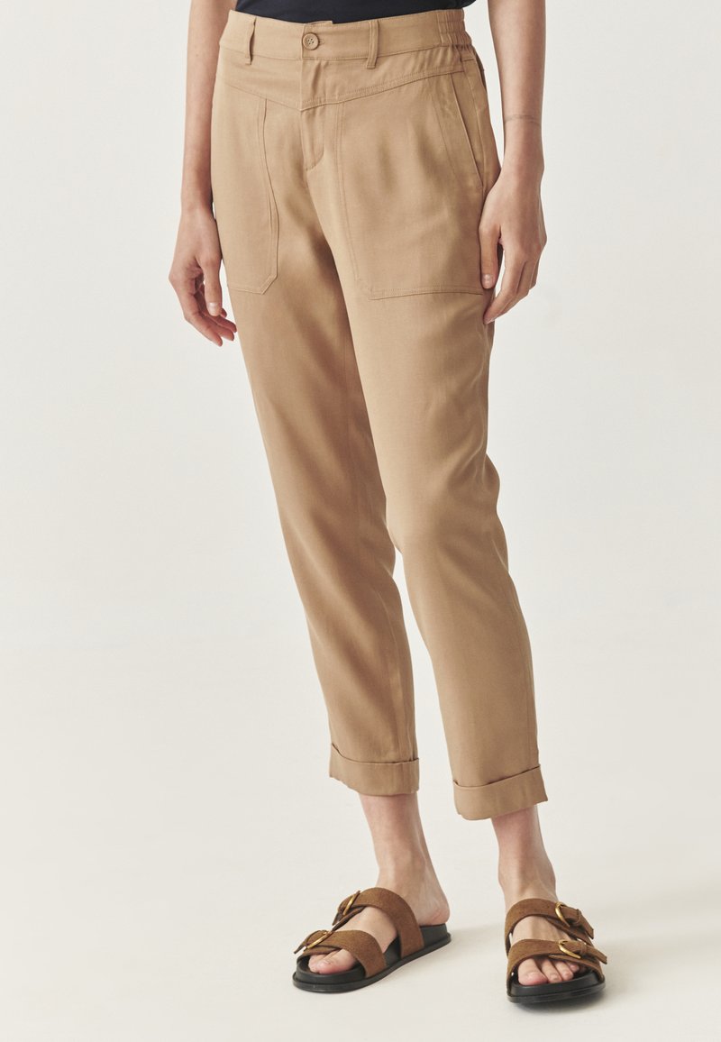 Khaki broeken met een taps toelopende pasvorm, voorzien van twee voorkruiken, een opgerolde zoom en een gladde textuur, gecombineerd met bruine sandalen.
