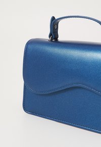 Blå metalisk håndtaske med rundet klap, tekstureret finish og syningsdetaljer. Har et kort håndtag til at bære med.