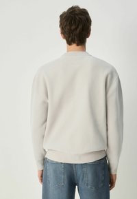 Lys grå, tekstureret crewneck sweatshirts med ribstrikkede manchetter og bund, båret sammen med blå jeans. Enkel, afslappet design med minimal detaljer.