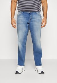 Ljusblå jeans med avslappnad passform, subtil blekning, femfickorsdesign och metalldesign, kombinerat med vita sneakers.