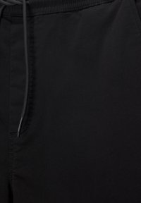 Shorts en tissu noir avec une texture lisse, une ceinture élastique avec cordon de serrage et des poches latérales avec des détails de couture discrets.