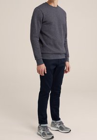 Sweatshirt gris texturé avec un col rond, associé à un pantalon bleu marine foncé et des baskets New Balance grises. Tous les vêtements sont ajustés.