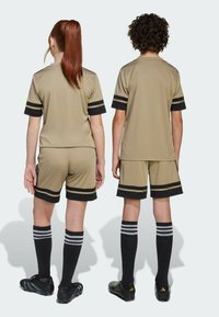 Uniformes deportivos beige con rayas negras, que incluyen una camiseta de manga corta y pantalones cortos. Medias negras hasta la rodilla completan el atuendo.