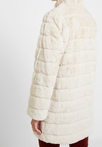 Faux fur-kappa i krämfärg, med en randig textur och hög krage, i en oversize-passform som når mitt på låret med vida ärmar.