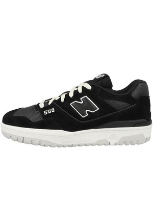 Black sneaker made of suede and leather, featuring a perforated design, white laces, and sole with tread, adorned with a large logo on the side.