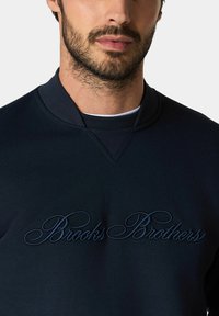 Granatowa bluza z teksturowanym wykończeniem i okrągłym dekoltem, z haftowanym napisem "Brooks Brothers" w kursywie z przodu.