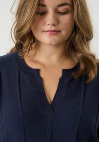 Tumesinine kootud topp V-kaelusega ja ribidega kraega. Omab vertikaalseid õmblusi ja tekstuuriga mustrit keskel. Pehme kangas.