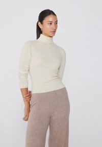 Cremfarbener, gerippter Strick-Turtleneck-Pullover mit langen Ärmeln, kombiniert mit weichen, hellbraunen, weit geschnittenen Hosen. Glatte Textur, figurbetontes Design.