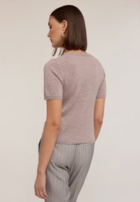 Krátký rukáv, světle růžový pletený svetr s kulatým výstřihem a jemnou strukturou. Nosený s šedými pruhovanými kalhotami, které vykazují těsný střih.