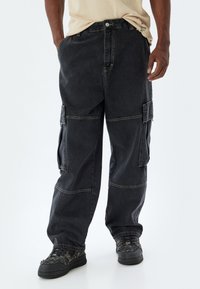 Svart cargobyxor med en lös passform, flera sidofickor och kontrasterande sömmar. Tillverkade av slitstark denim med en lätt textur.
