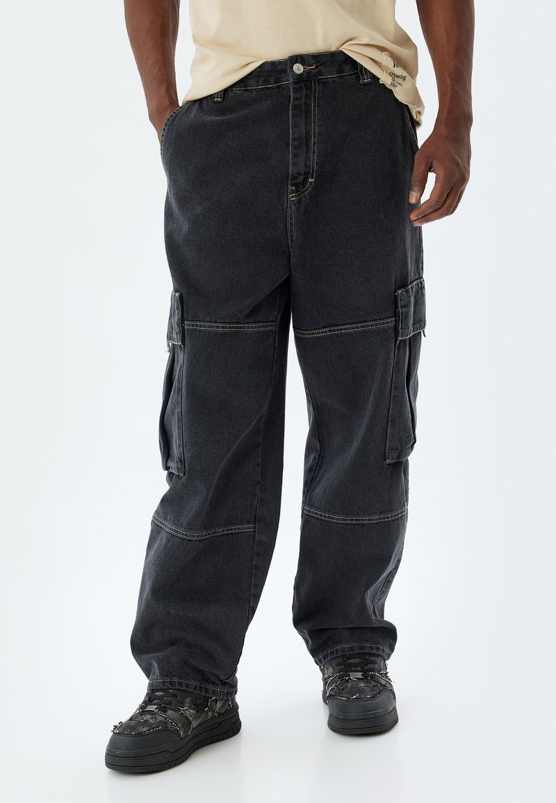 Svart cargobyxor med en lös passform, flera sidofickor och kontrasterande sömmar. Tillverkade av slitstark denim med en lätt textur.