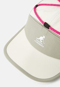 Cappello chiaro con una visiera ampia, caratterizzato da una combinazione di grigio e crema. Include un cordino accentato in rosa e un logo Kangol bianco.