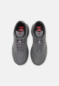 Baskets de sport grises avec un dessus lisse, des lacets texturés et des semelles en caoutchouc. Comprend un logo rouge sur la languette et des coutures contrastées.