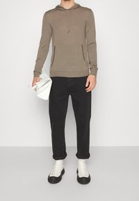 Khaki huvtröja med en framficka i kängurustil, kombinerad med svarta jeans och vita sneakers med svarta sulor. Slät textur, avslappnad passform.