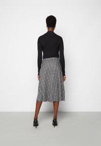 Černý top s dlouhým rukávem ve spojení s šedou károvanou midi sukní. Sukně má rozšířený tvar a je zakončena lemem nad kotníky.