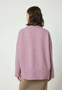 Rožinė, pūkuota megztinis su laisvu kirpimu, rauktomis rankovėmis ir plačiomis rankovėmis. Minkštas audinys, aukšta apykaklė ir paprastas dizainas.