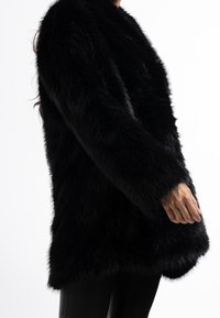 Černý kabát z umělé kožešiny s dlouhými rukávy, měkkou texturou a volným střihem, s zaobleným předním okrajem a bez viditelných zapínání.
