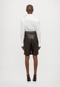 Hvit skjorte med lange ermer, stappet inn i mørkebrune skinnshorts med elastisk midje og baklommer, båret med svarte hæler.