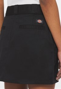 Svart denimkjol med midjeband och två bakfickor. Har en logotypklistermärke på högra sidan. Slät textur, A-linjeformad design.