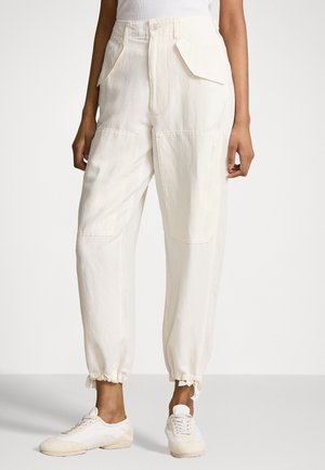 Witte broek met hoge taille, grote voorzakken en elastische enkels, gedragen met witte sneakers en een wit topje.
