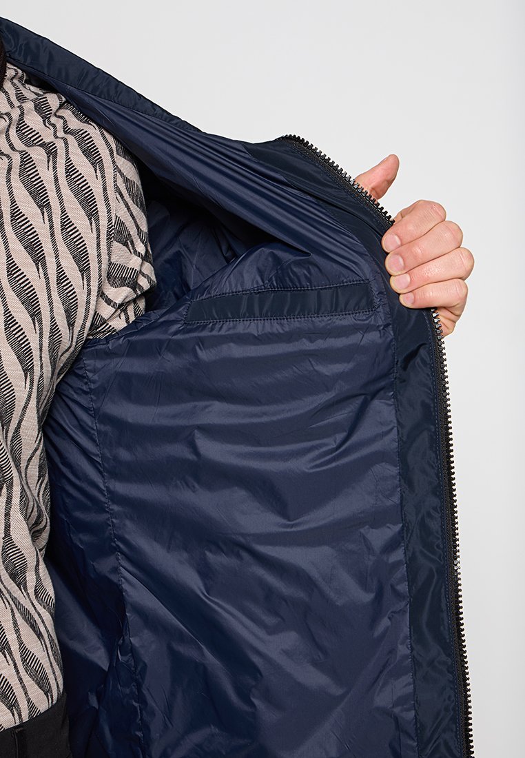 Eine Person trägt ein Hemd mit Zebramuster und hält eine dunkelblaue Jacke offen, um das glatte Innenfutter und die Innentasche zu zeigen.