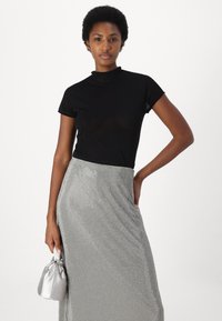 Black short-sleeve top with a high neck, paired with a shiny silver rhinestone-embellished skirt and a small silver handbag.
