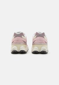 Sapatilhas em camurça rosa, com uma entressola branca e bege, incluindo uma camada transparente. Apresentam uma sola preta sólida e detalhes texturizados.