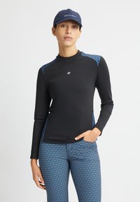 Maglia sportiva nera a maniche lunghe con accenti blu a motivo sulle spalle, abbinata a leggings blu a motivo con design geometrici.