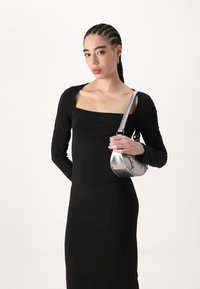 Juoda ilga rankovė su kvadrato formos iškirpte, derinama su metalizuota sidabrine rankine. Rankinė turi išlenktą formą ir dekoratyvinius akcentus.