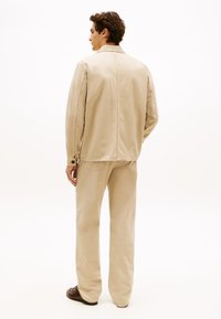 Beige Baumwolljacke mit geradem Schnitt und Seitentaschen, kombiniert mit passenden Hosen. Glatte Textur, minimalistisches Design und dezente Nähte.