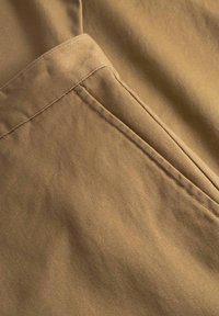 Tissu en coton beige avec une texture lisse, présentant une couture détaillée et un pli diagonal, créant une apparence élégante et épurée.