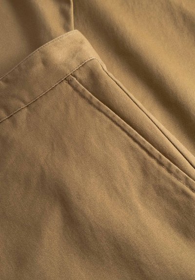Tissu en coton beige avec une texture lisse, présentant une couture détaillée et un pli diagonal, créant une apparence élégante et épurée.